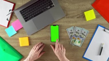 Worker is showing how easy to earn money with freelance green screen mockup. American value. 100 dollar bills. Laptop, color stickers and notebooks. Phone in vertical position.