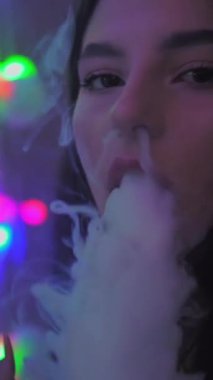 The girl smokes a vape releases a lot of steam. Color light. Vertical video. High quality FullHD footage