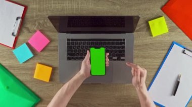 Freelancer is showing on the phone in vertical position how easy to earn money with freelance green screen mockup. Laptop, color stickers and notebooks.