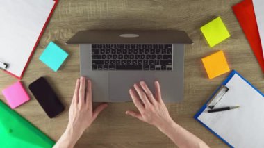 Student is scrolling down on the touchpad. Phone, color stickers and papers on the table.