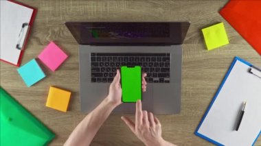 The coder is showing the programming courses on the phone green screen mockup concept. Vertical position. Workplace with laptop, color stickers, files.
