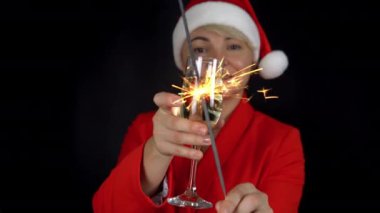 Bir kadeh şampanyayla neşeli yetişkin kadınlar. Gülümseyen mutlu kadınlar siyah arka planda bengal ateşi sallıyor.. 