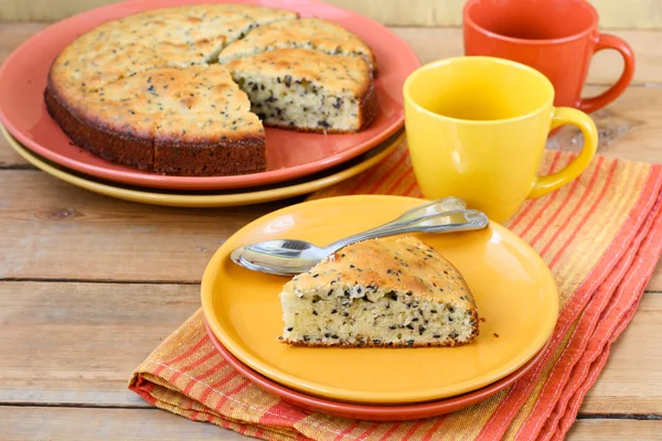 Kuchenstück mit schwarzem Sesam, serviert auf dem Holztisch mit bunten Tellern und Tassen — Stockfoto