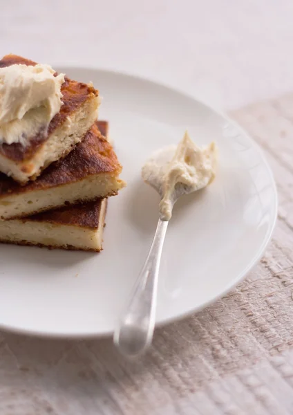 Cheesecake på en rund platta och en sked med grädde — Stockfoto