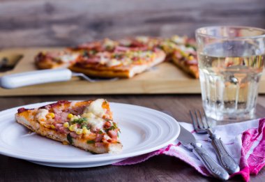 Pizza dilimleri bir tabak, beyaz masa ve bir çatal bıçak takımı