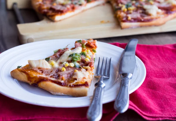 Pizzascheiben auf einem Teller, weißer Tisch und Besteck — Stockfoto