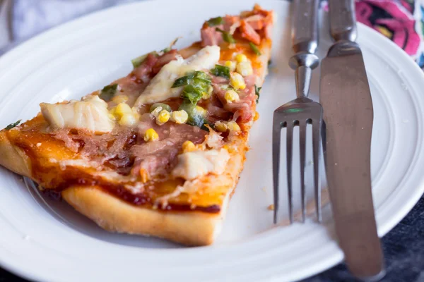 Pizzascheiben auf einem Teller, weißer Tisch und Besteck — Stockfoto