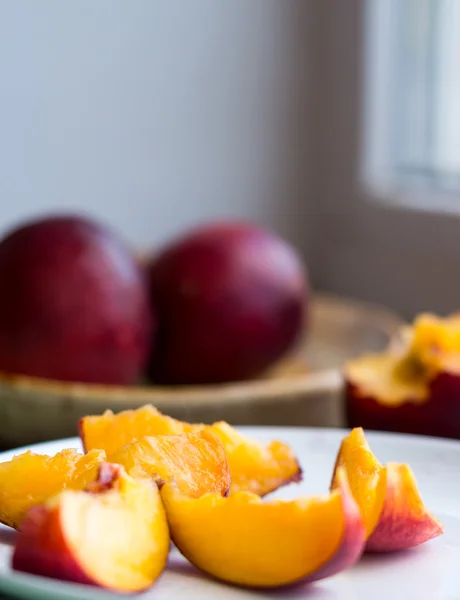 Peaches, juicy slices on white round plate, window — Stock Photo, Image