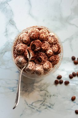 Mini masadaki plastik bardaklarda atıştırmalıklar. Tiramisu, beyaz mermer arka planda geleneksel İtalyan tatlısı.