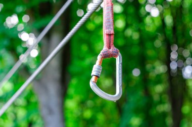 Safety harness with a carabiner on a cable. The bridges, ropes and ladders of the Adventure Park are designed for beginners among the tall trees.