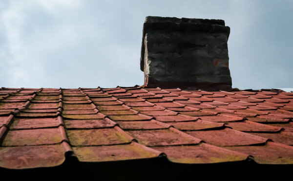 Fragment of a roof with a chimney and a cloudy sky. Material - old red metal tile.