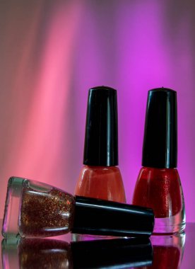 Güllerde üç tırnak cilası ve kırmızı arka plan. Biri mercan cilası, diğeri kırmızı ve üçüncüsü ise kırmızı ve altın parıltılarla kaplı.