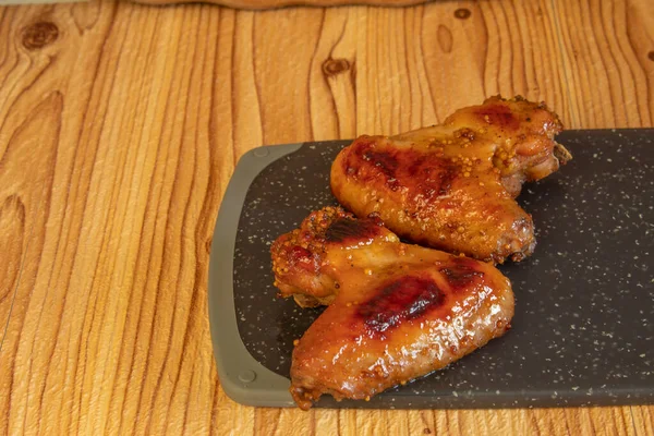 Baked two chicken wings with honey and mustard on a dark cutting board. Copying text or logo.