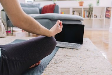 Evinde bilgisayarıyla yoga yaparken tanınmayan bir kadının eline yakın çekim yapmak. Fitness konsepti.