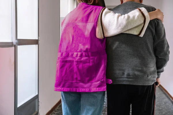 Genç bir sağlık gönüllüsü yaşlı bir adamın bastonla yürümesine yardım etmek için kollarını koruyucu bir şekilde üzerine koyuyor. Bakım anlayışı. Yaşlanma konsepti. Gönüllü olma konsepti. Boşluğu kopyala