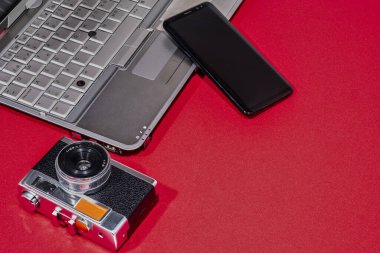 Kompozisyon, dizüstü bilgisayar, kamera ve kırmızı masanın üstünde bir cep telefonu