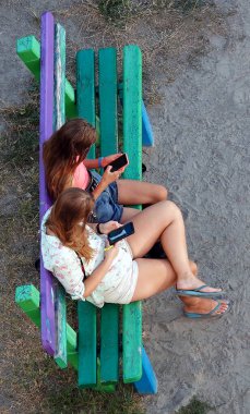 Kiev, Ukraine August 17, 2020: Two girls are watching the phone while sitting on a bench