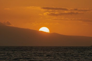 Maui plajından sihirli altın gün batımı, deniz ve dağ arka planı. 