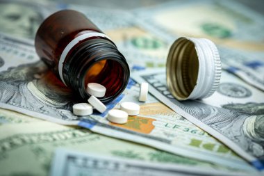 100 dolarlık banknotların üzerinde hap olan ilaç şişesi. Para ve sağlığın bir arada olduğu tıp endüstrisi.