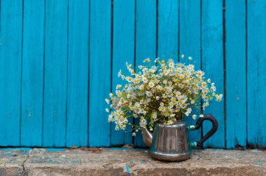 Tahta bir arka planda, demir bir vazoda, beyaz papatyalar.