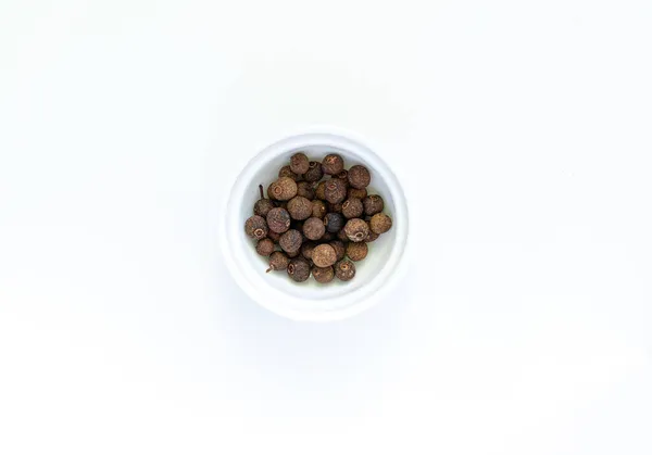 Ολόκληροι αποξηραμένοι μαύροι κόκκοι πιπεριού σε στρογγυλό άσπρο μπολ σε λευκό φόντο — Φωτογραφία Αρχείου