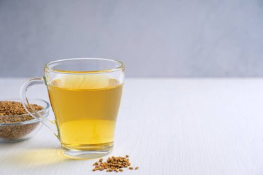 Mısır 'ın yerel tıbbında ve gıda malzemesi olarak kullanılan mutfakta, beyaz ahşap masa üzerinde bir kase tohumla birlikte cam fincanda servis edilen helba ya da altın çay. Kopyalama alanı olan resim