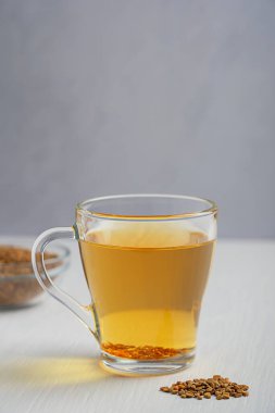 Mutfakta gıda malzemesi olarak kullanılan gri duvara karşı beyaz ahşap arka planda tohumlarla servis edilen cam fincanda servis edilen çam ağacından yapılmış Helba altın çayı içeceği. Kopyalama alanı olan dikey resim