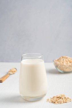 Kahvaltıda beyaz ahşap masada kahvaltıda yulaf lapası ve kaşıkla servis edilen yulaf ezmesi tadında vejetaryen bitki sütü, laktoz ve süt ürünleri. Kopyalama alanı ile, dikey