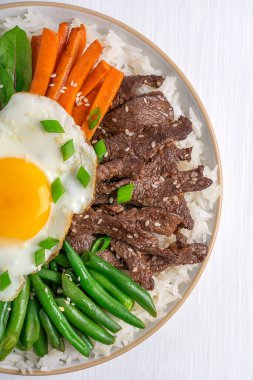 Bibimbap 'ın, sebze, dilimlenmiş et, havuç ve sarı yumurta ile kaplanmış, soğan ve susam tohumlarıyla tatlandırılmış, bibibimbap popüler pirinç yemeğinin üst görüntüsü.