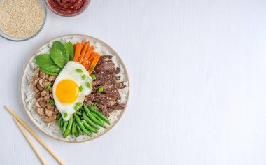 Sığır eti dilimleri, sebzeler ve yumurta sarısı ile kaplanmış haşlanmış pirinçten yapılmış Asya Bibimbap tabağının hemen üstünde.