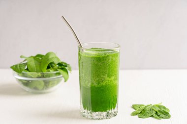 Yeşil organik vejetaryen ev yapımı ıspanaklı smoothie ya da kahvaltıda pipetle servis edilen meyve suyu ve kahvaltıda beyaz ahşap masa malzemesi. Sağlıklı diyet kavramı