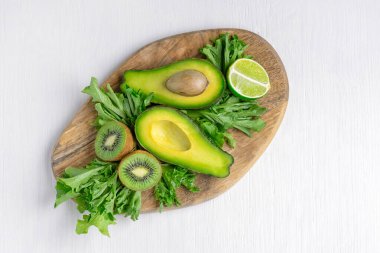 Çeşitli yeşil çiğ sebze ve meyvelerin üst görüntüsü ve beyaz ahşap masanın üzerinde duran avokado, elma, limon, marul ve kivi gibi bütün. sağlıklı vejetaryen diyet konsepti
