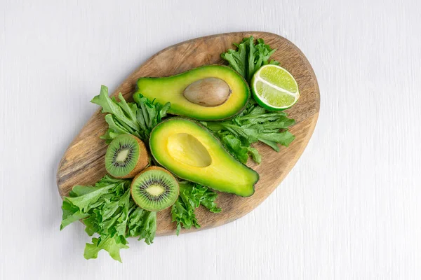 Çeşitli yeşil çiğ sebze ve meyvelerin üst görüntüsü ve beyaz ahşap masanın üzerinde duran avokado, elma, limon, marul ve kivi gibi bütün. sağlıklı vejetaryen diyet konsepti