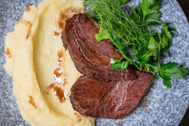 Izgara veya ızgara sığır eti, sulu biftek, yeşil dereotlu ve maydanozlu ve restoranda akşam yemeği için gri tabakta servis edilen soslu haşlanmış patates püresi.