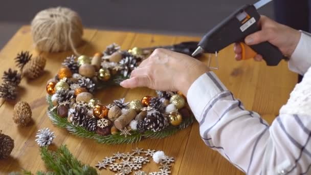 Les mains féminines décorent la couronne de Noël avec un décor à l'aide d'un pistolet à colle. Fleuriste au travail. — Video