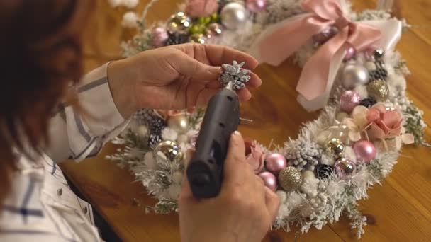 Női kéz díszíteni a karácsonyi koszorú egy dekoráció ragasztópisztollyal. — Stock videók