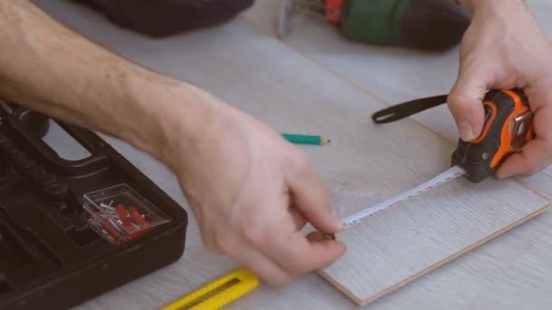 Zbliżenie stolarza instalowanie nowej laminowanej podłogi drewnianej. Dłonie pracowników mierzą deskę laminowaną. — Wideo stockowe