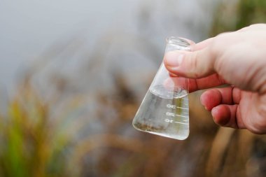Müfettiş elinde nehir suyuyla kimyasal bir şişe tutuyor. Enfeksiyon için su testi.