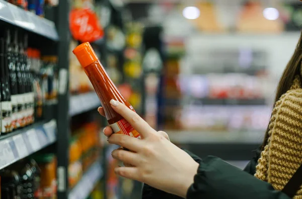 Female hand choosing natural red chili pepper sauce at store. — стоковое фото