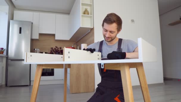 Smiling busy man in construction uniform assembles table with screwdriver, work with pleasure in living room. — Stock Video