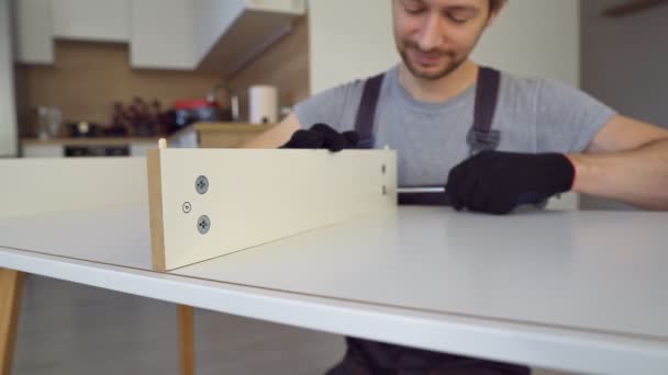 Close up of man worker in construction uniform assembles table with screwdriver. — Stock video