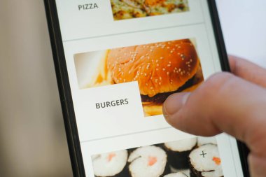 Ekranda uygulamalı akıllı telefon kullanarak erkek ellerini kapat. Hamburger seçen genç adam..