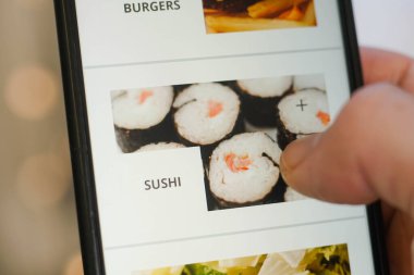 Ekranda uygulamalı akıllı telefon kullanarak erkek ellerini kapat. Suşi seçen genç adam..