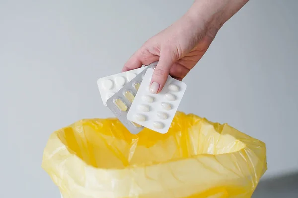 Womans hand throws expired blister pills to the trash bin. Stock Photo