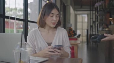 Elektronik ödeme makinesinden ya da kart okuyucudan ödemeyi telefonla yapın. Nakitsiz cüzdanda e-para. Çalışan ve cep telefonu çekimleri yapan kadın elleri var. Müşteri kahveciden yemek ısmarlar..