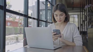 Kahve dükkanında akıllı telefon kullanan genç bir kadın, mutlu bir gülümseme..
