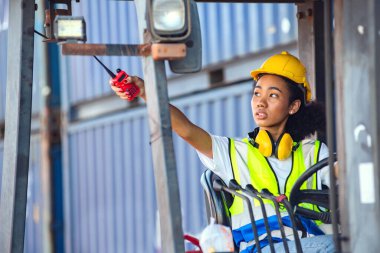 Kadın ustabaşı, konteynır deposunda forklift kullanırken telsiz iletişimini kullanıyor. Rıhtımda nakliye.