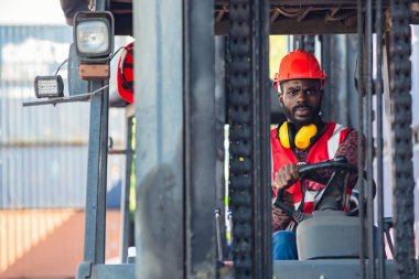 Üniformalı, kask takan ve ticari liman alanında dizel konteyner forklift kullanan bir erkek işçi..