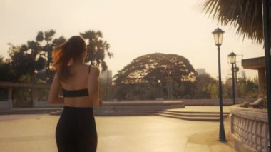 Gün batımında şehirde spor kıyafetleriyle koşan bir kadın..