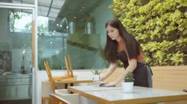 Bir bayan restoran çalışanı ya da genç girişimci müşterileri karşılamak için yemek masasını temizler..